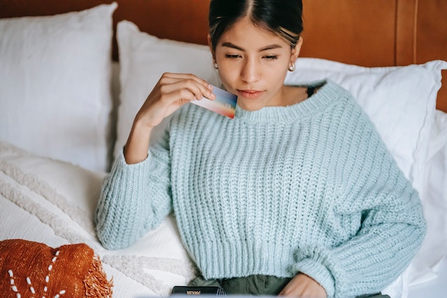 person sitting in bed holding a credit card making a payment