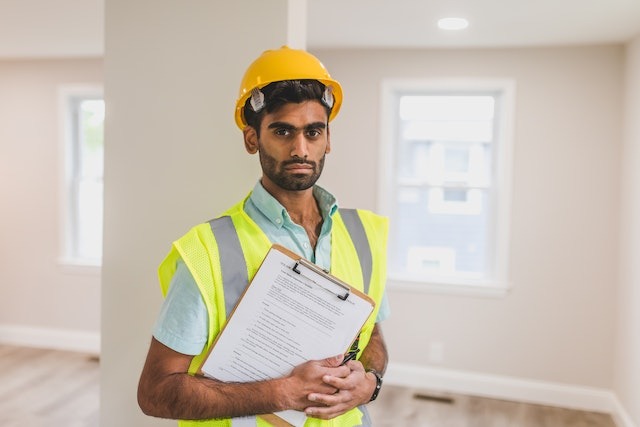 person with clipboard and hard hat inspecting a home