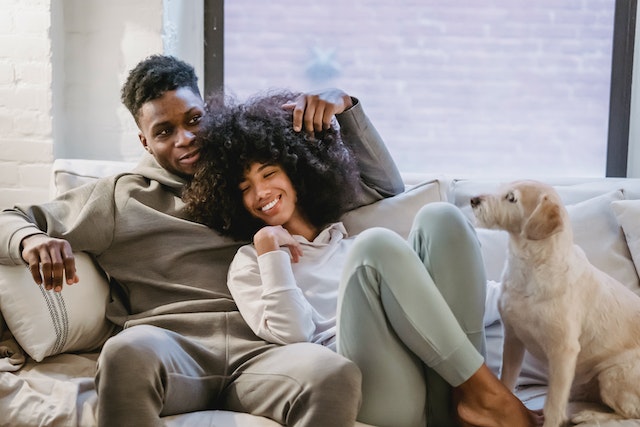 two people sitting on a couch with a dog