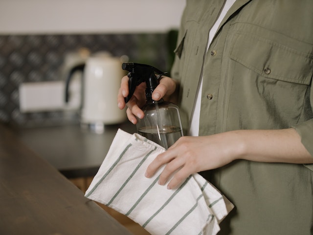 a person holding a rag and spray bottle near a counter