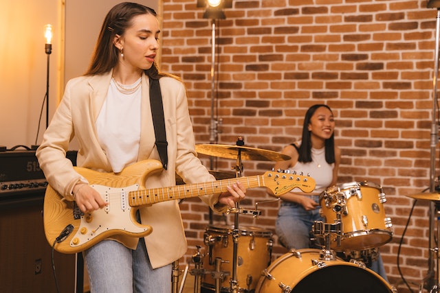 one person playing a guitar and another playing the drums indoors
