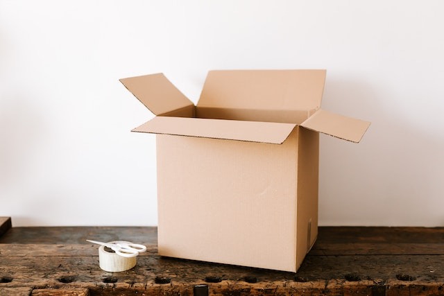 a moving box next to tape and scissors on a table