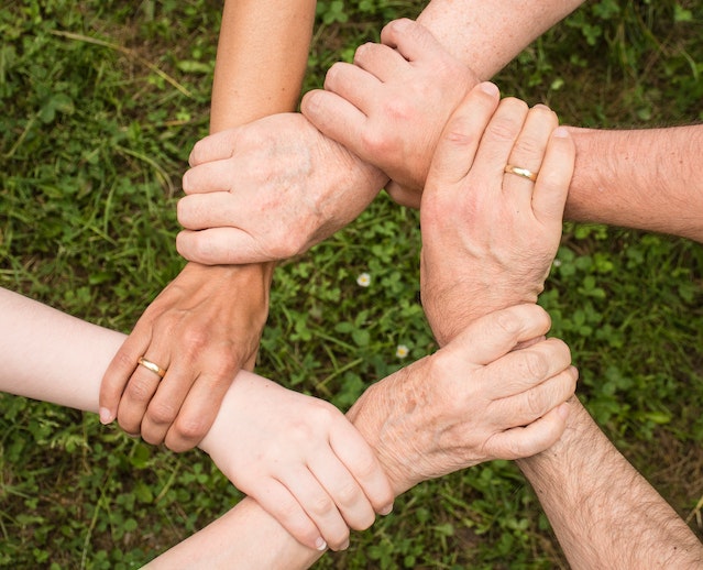 three pairs of hands holding wrists in a circle