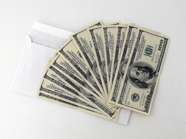 several hundred dollars of us currency sit on top of an envelope